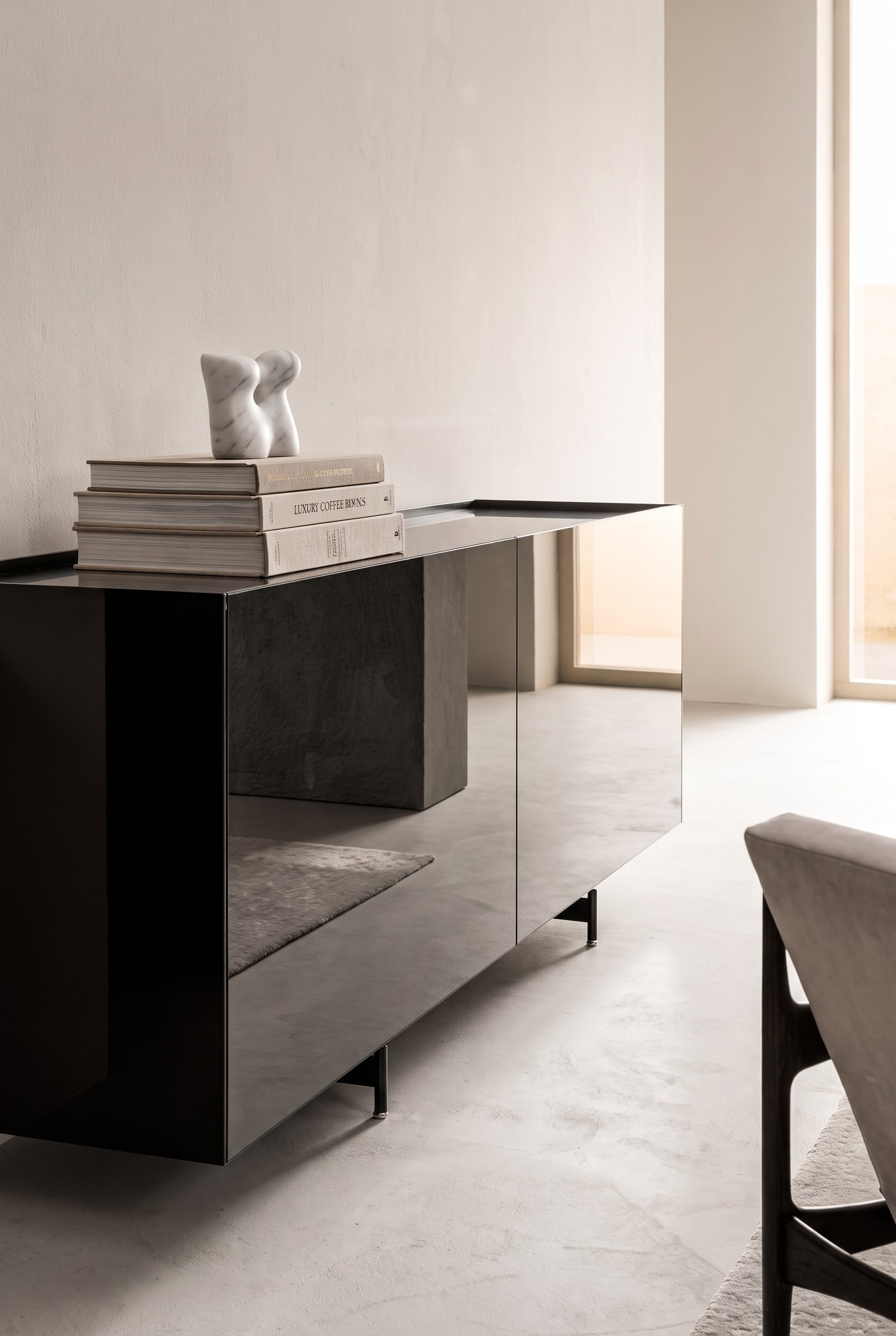 Sideboard mit verspiegelten Fronten, darauf ein ordentlicher Stapel aus drei großen Bildbänden, gekrönt von einer kleinen weißen Marmorskulptur