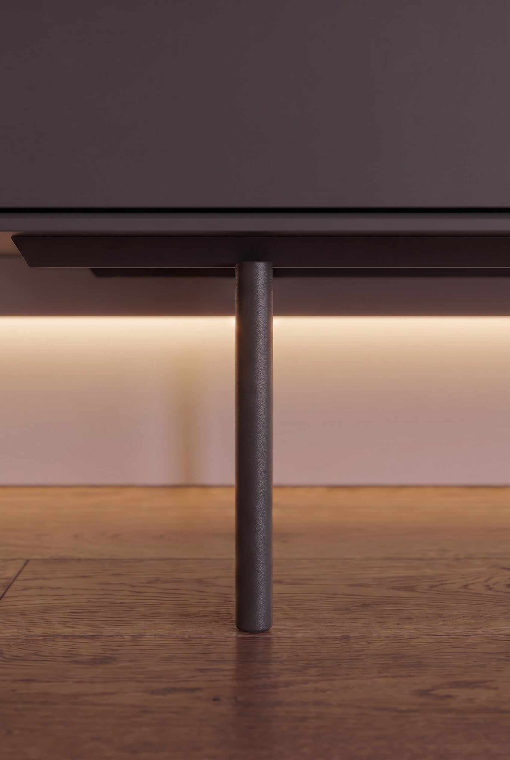 Nahaufnahme eines schmalen, zylindrischen Metallfu&szlig;es eines Sideboards mit indirekter Unterbodenbeleuchtung auf Holzparkett.