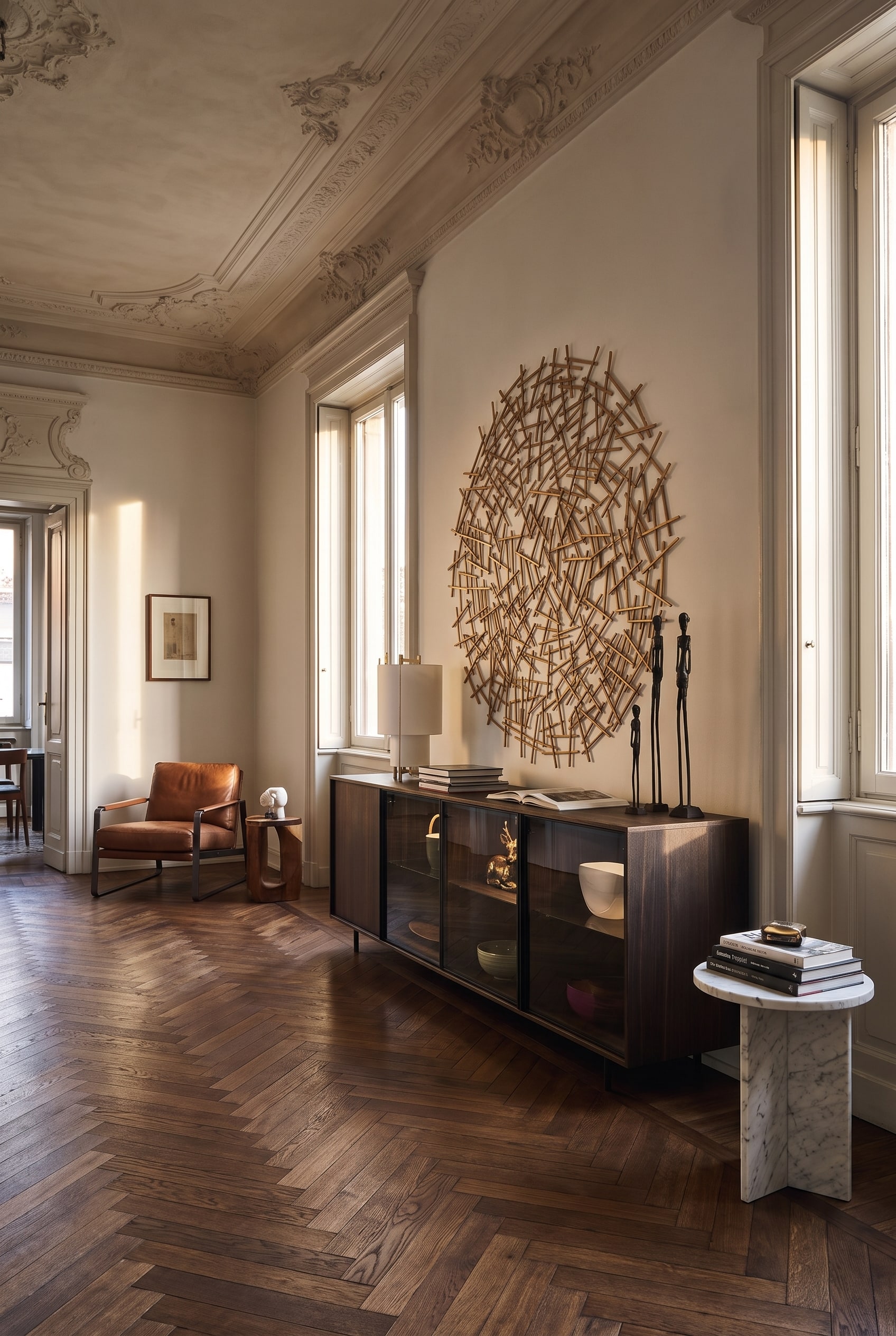 Ein langgestrecktes Glas-Sideboard auf schwarzen Metallkufen an einer Wand in einem Altbauzimmer, unter dem das Eichen-Fischgrätparkett ununterbrochen weiterläuft.