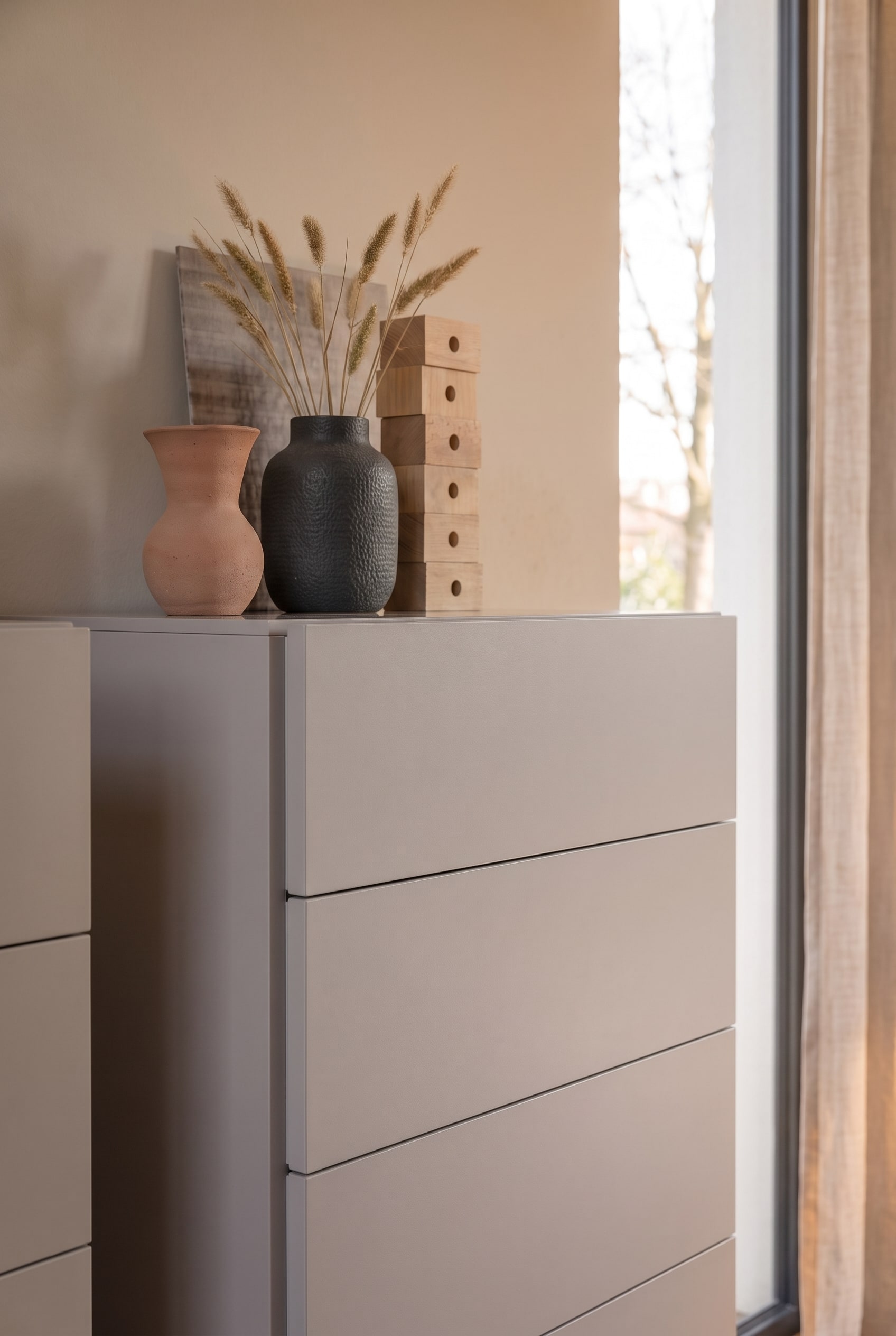 Nahaufnahme einer greigen Kommode, dekoriert mit Terrakotta-Vasen, dunkler Keramik und getrockneten Gräsern.