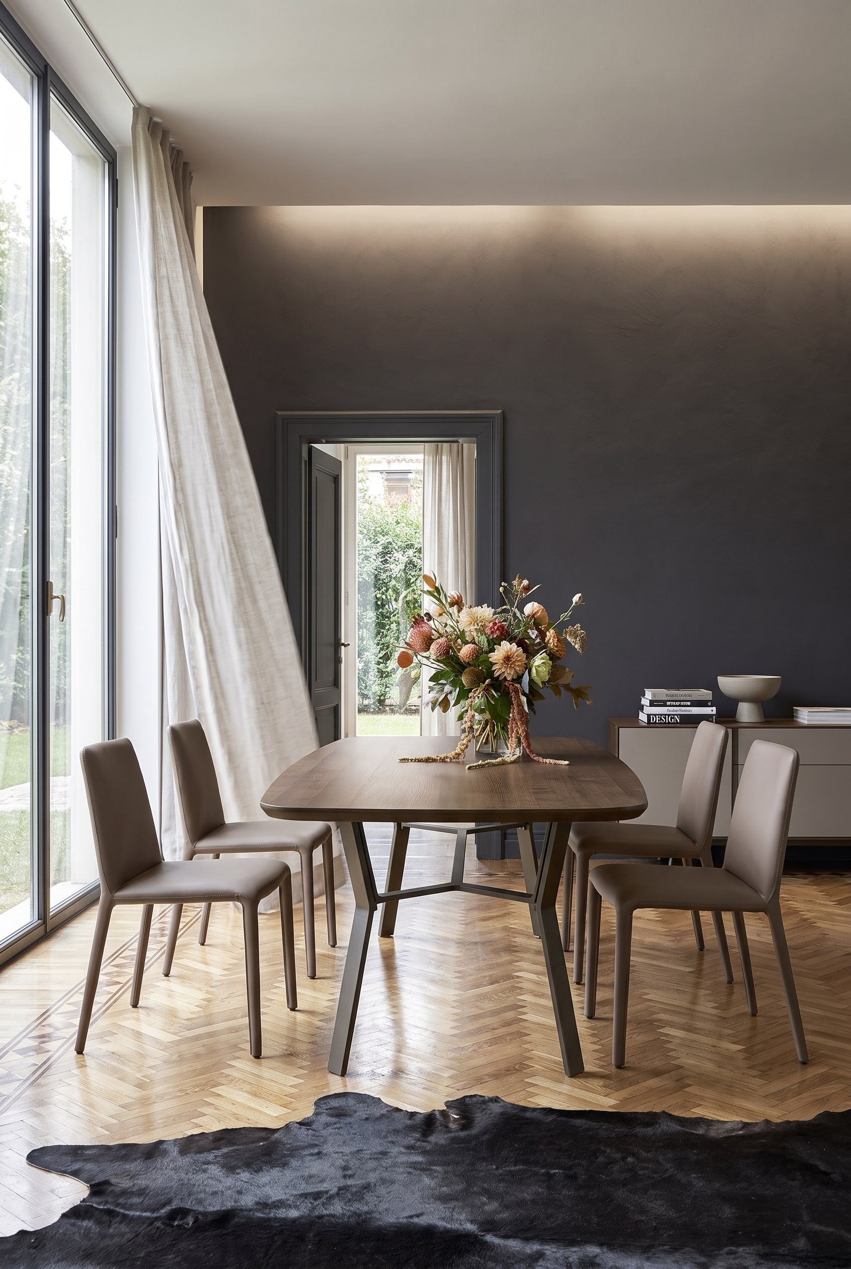 Minimalistisches Esszimmer mit dunkler Akzentwand, Holztisch auf Eisengestell und vier taupefarbenen Lederstühlen