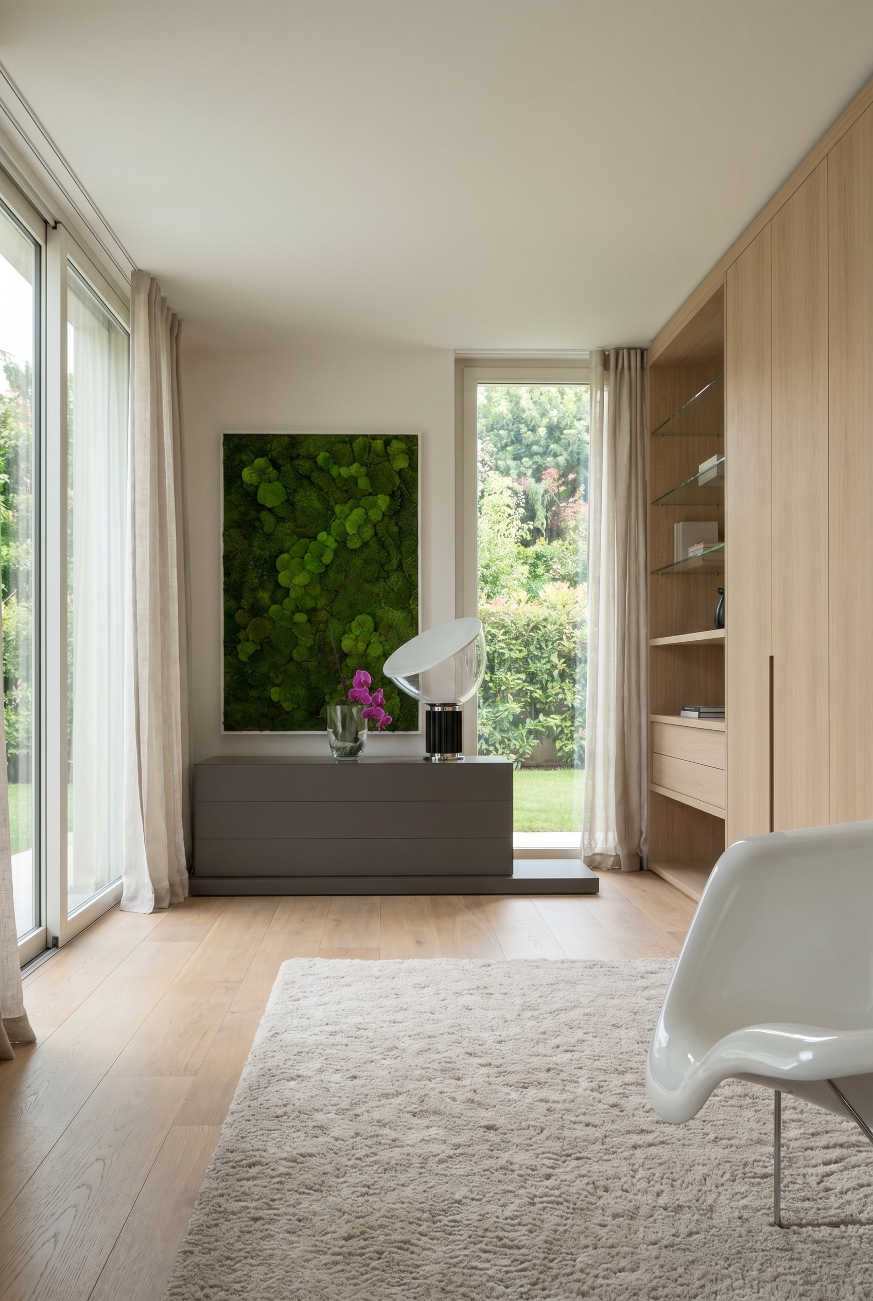 Elegantes Schlafzimmer mit niedriger, dunkelgrauer Kommode, darüber ein Moosbild und ein weißer Schalenstuhl