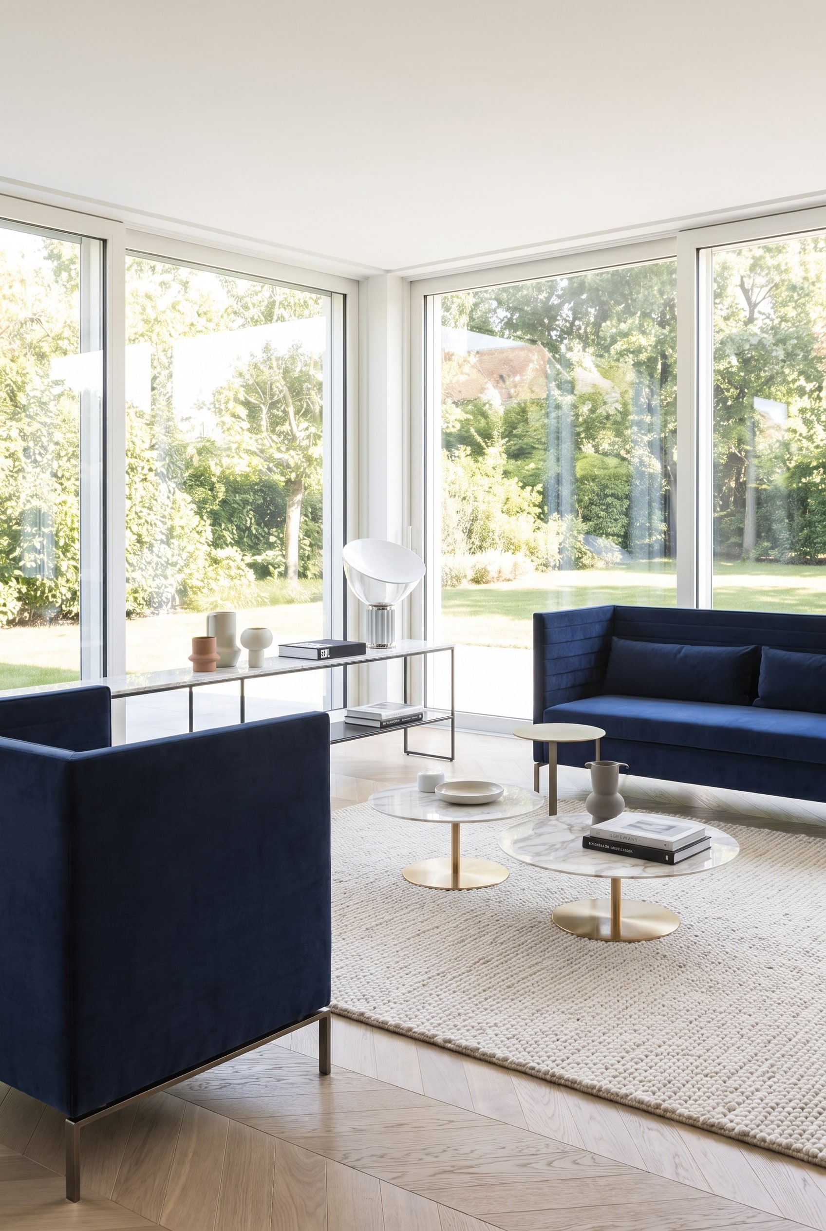 Gro&szlig;z&uuml;gig wirkendes Wohnzimmer mit einem dunkelblauen, filigranen Sofa auf schlanken Metallkufen, das den hellen Holzboden sichtbar l&auml;sst.