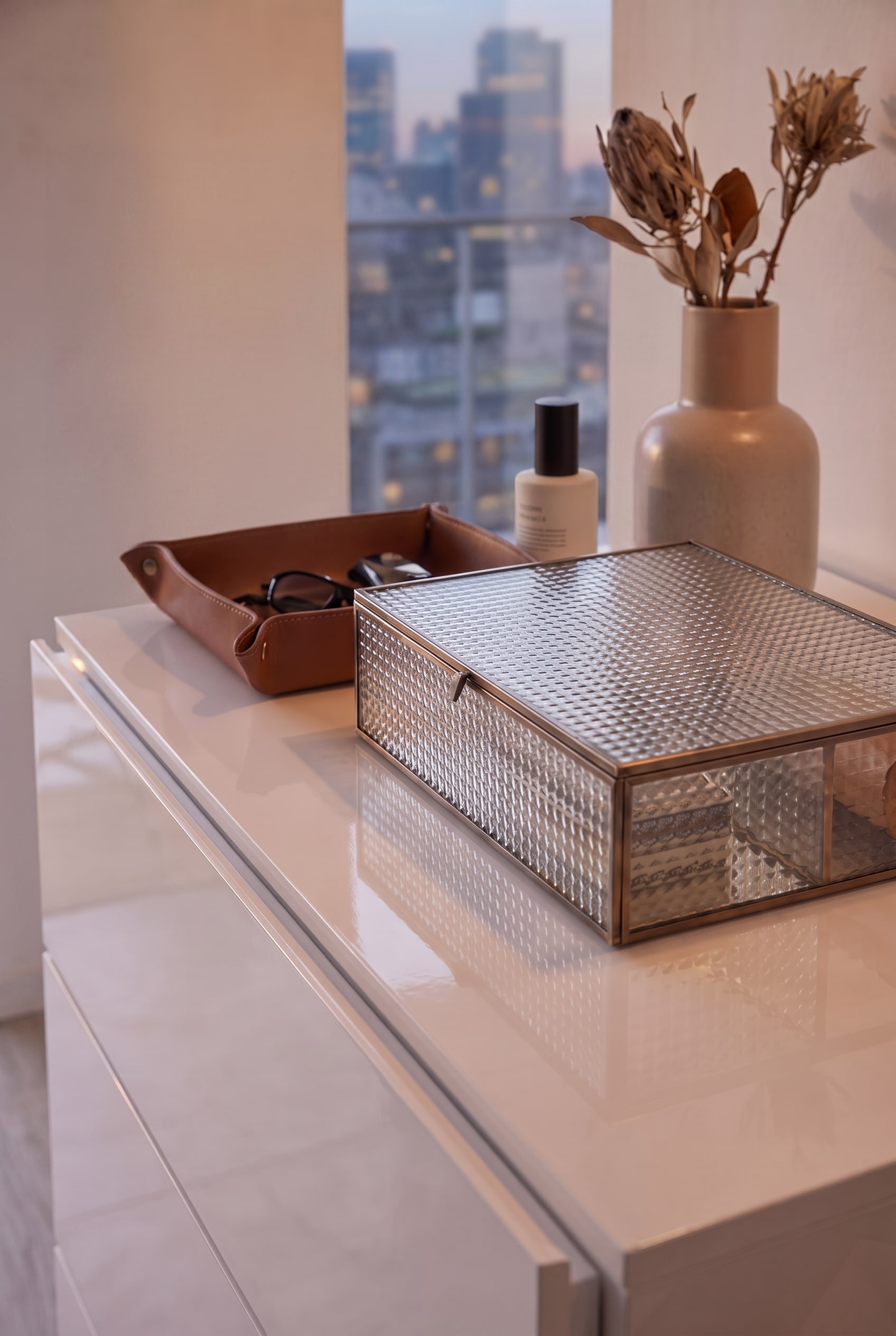 Draufsicht auf eine weiße Hochglanzkommode mit Glasbox und Lederschale, puristisch ohne Garderobenstange inszeniert.