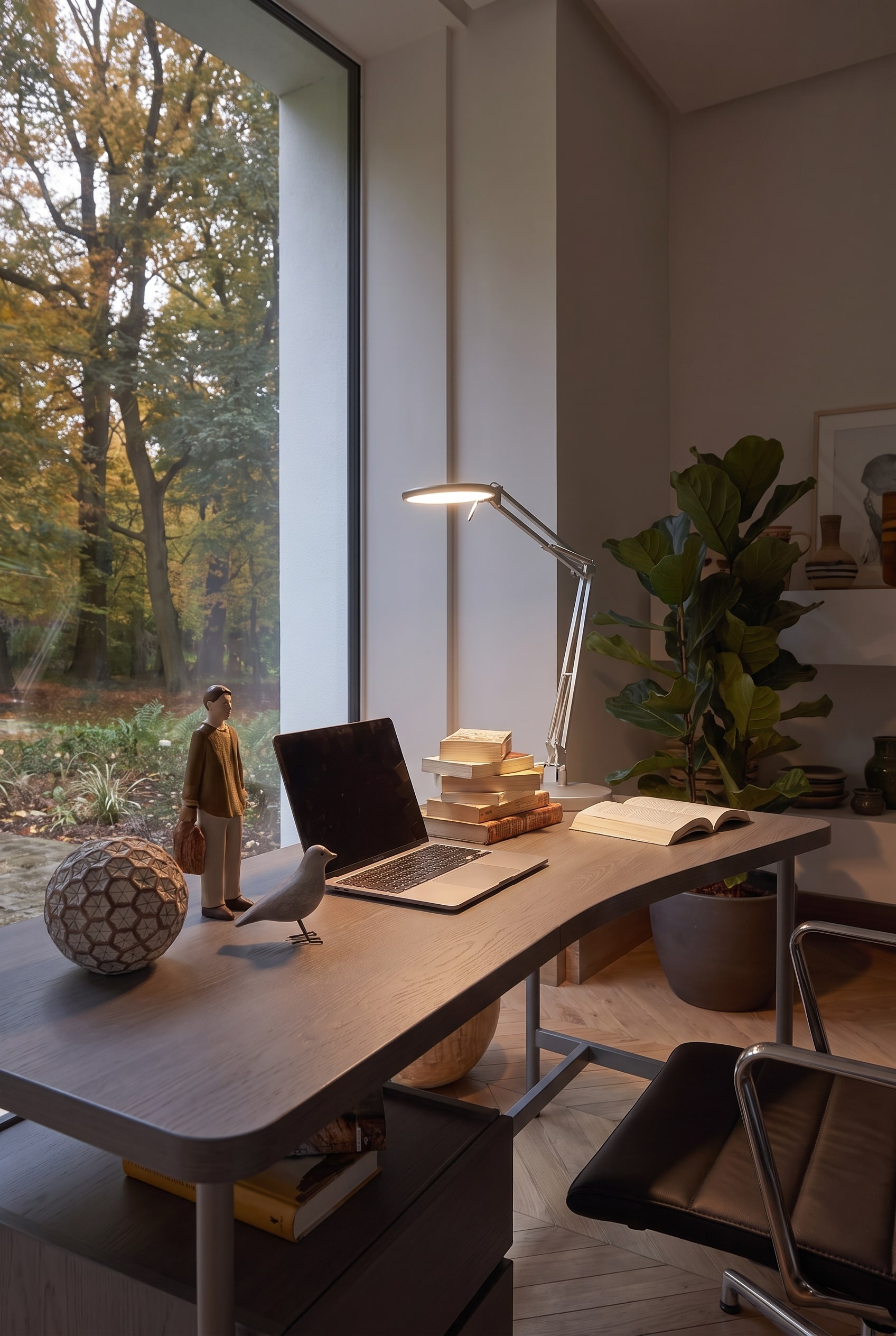 Beleuchteter Arbeitsbereich auf dem Schreibtisch mit gl&auml;nzender Chromlampe, Holzfiguren und Laptop.