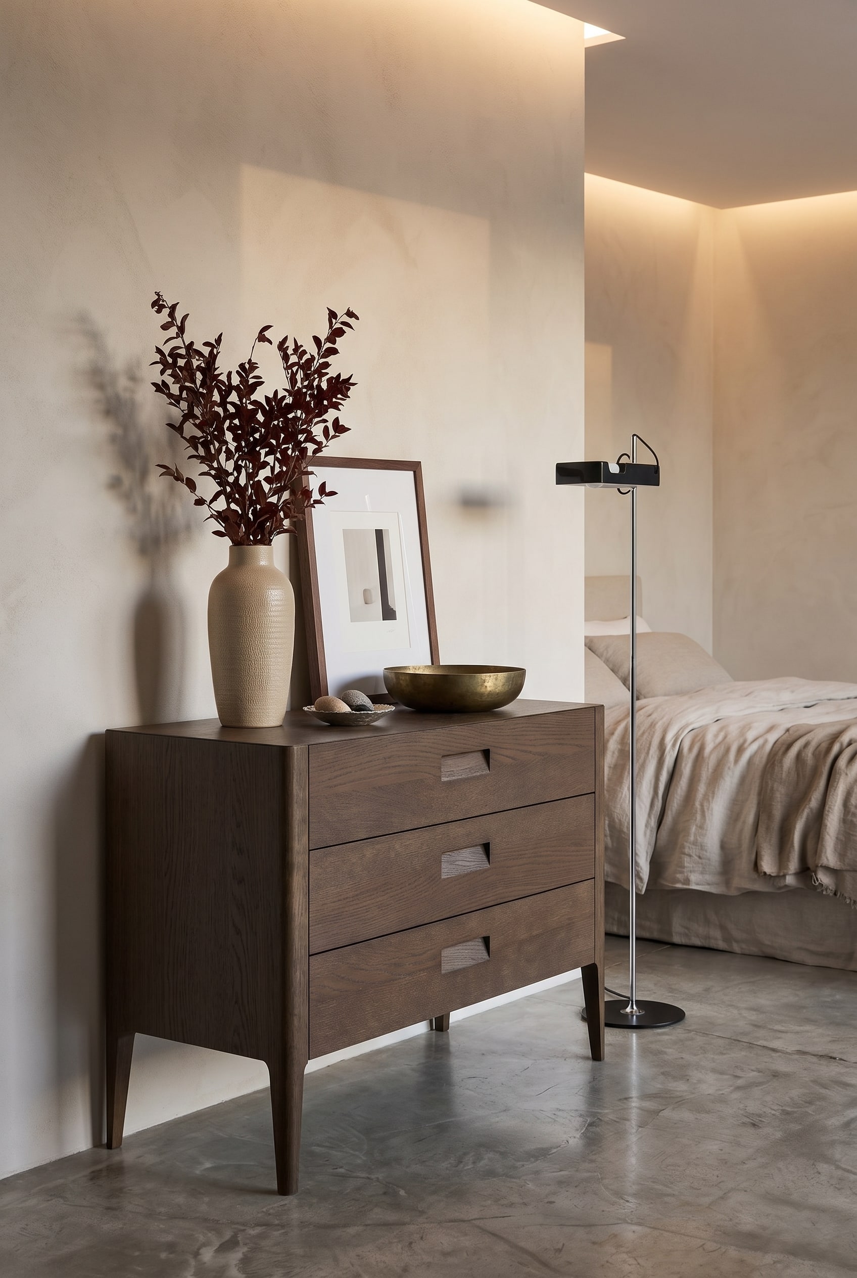 Modernes Schlafzimmer mit dunkler Eichenholz-Kommode, hoher Keramikvase, mittelgro&szlig;em Bilderrahmen und flacher Messingschale in warmem Licht
