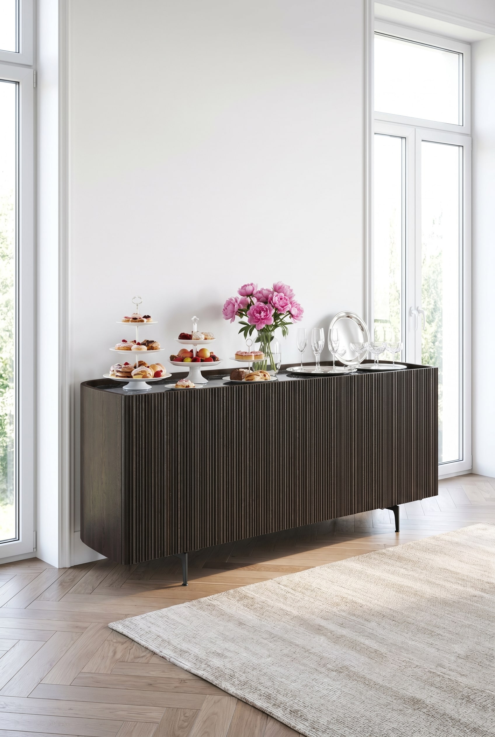 Dunkles Novamobili Bay Sideboard mit abgerundeten Ecken und geriffelter Front in einem hellen Raum, dekoriert mit wei&szlig;en Porzellantellern und rosa Pfingstrosen.