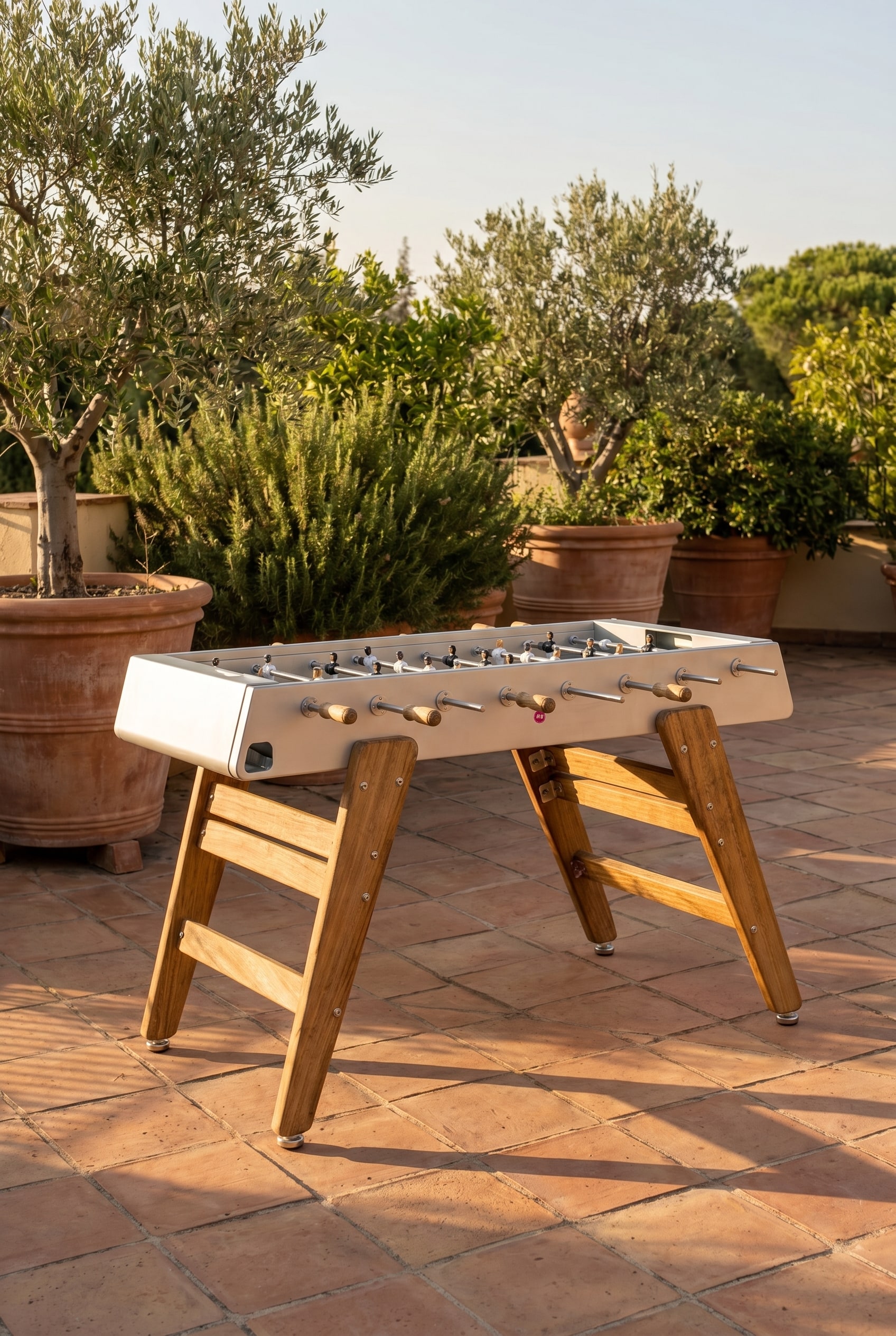 Mediterrane Terrasse mit Iroko-Holz Tischkicker und großen Pflanzkübeln im warmen Abendlicht
