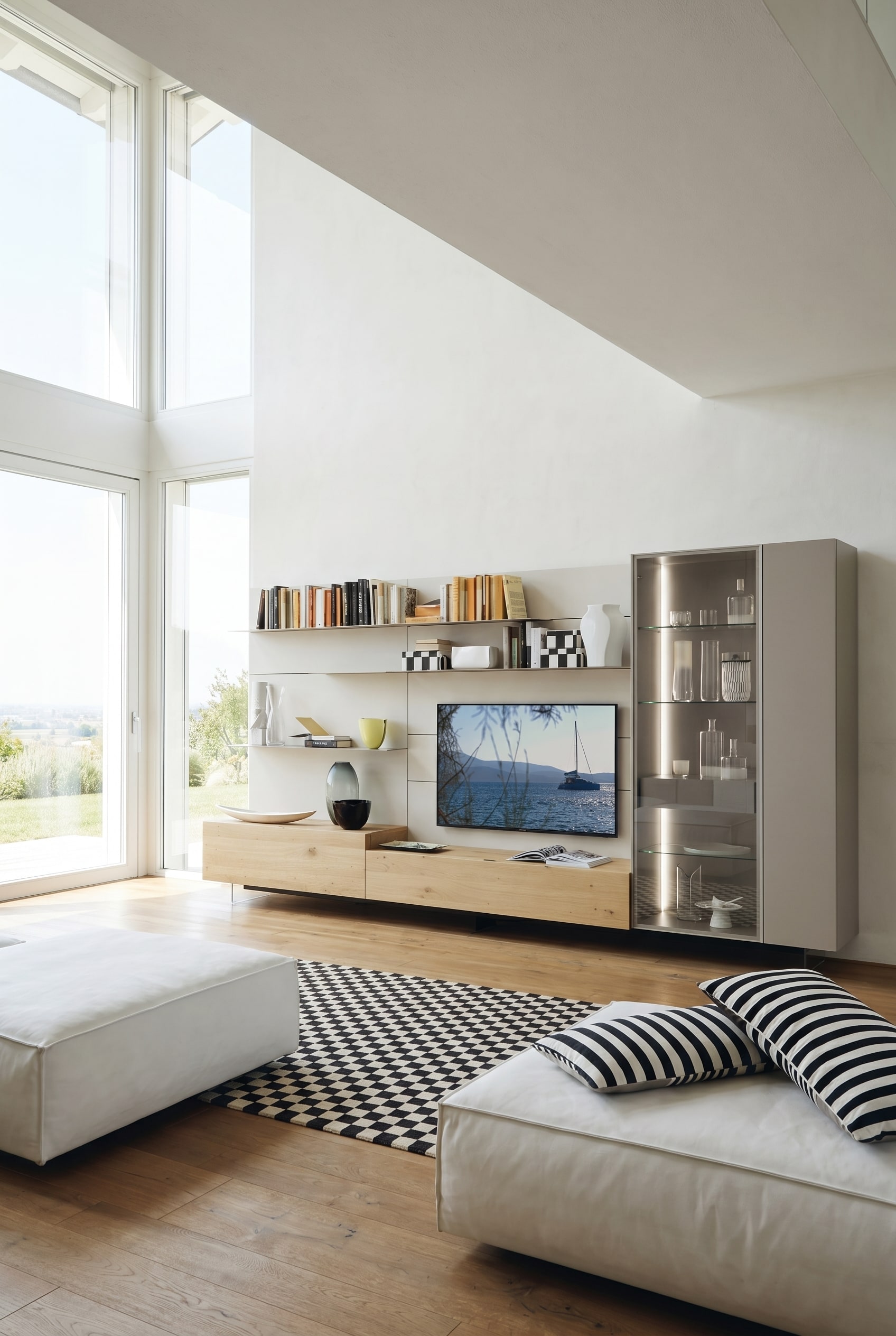 Helles Wohnzimmer mit schwebenden Basismodulen aus heller Eiche, weißen Regalböden und einer hohen, warm beleuchteten Glasvitrine