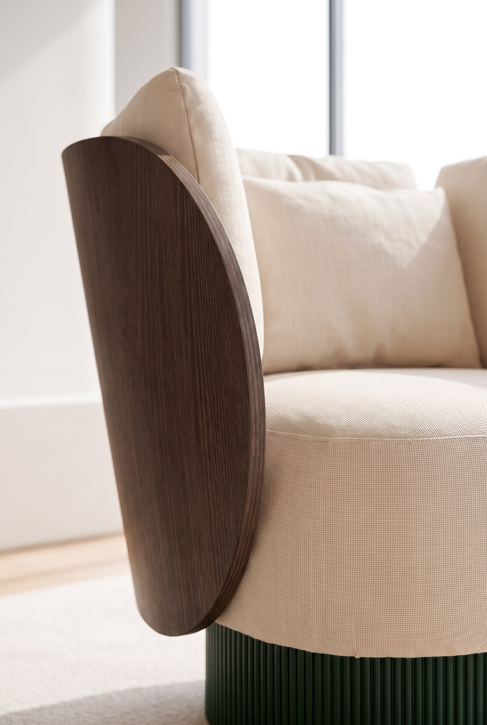 Nahaufnahme der Materialkombination aus gebogenem Holz, gerilltem Sockel und beigem Premium-Stoff.
