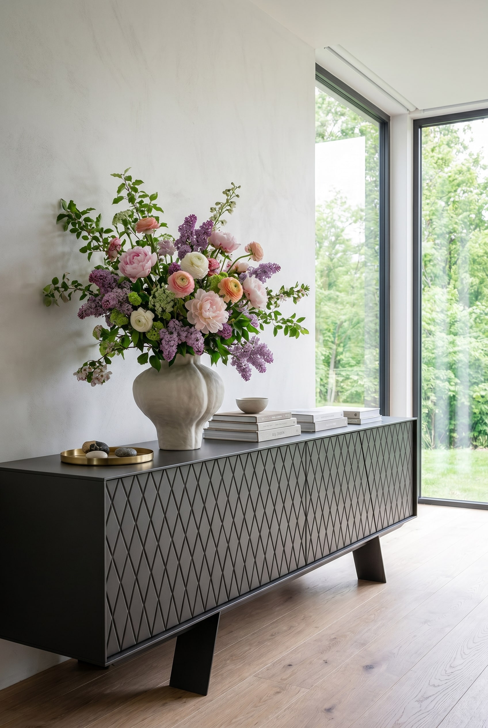 Minimalistisches Wohnzimmer mit bodentiefen Fenstern, hellem Tageslicht und einem eleganten niedrigen Sideboard, auf dem eine volumin&ouml;se Fr&uuml;hlingsvase steht