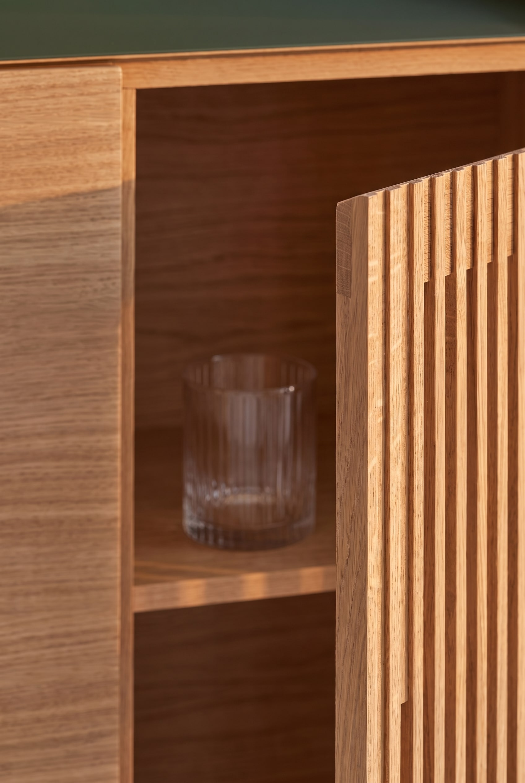 Makroaufnahme der Lamellenfront eines Highboards aus heller Eiche, durch den Spalt ist ein Glas sichtbar.