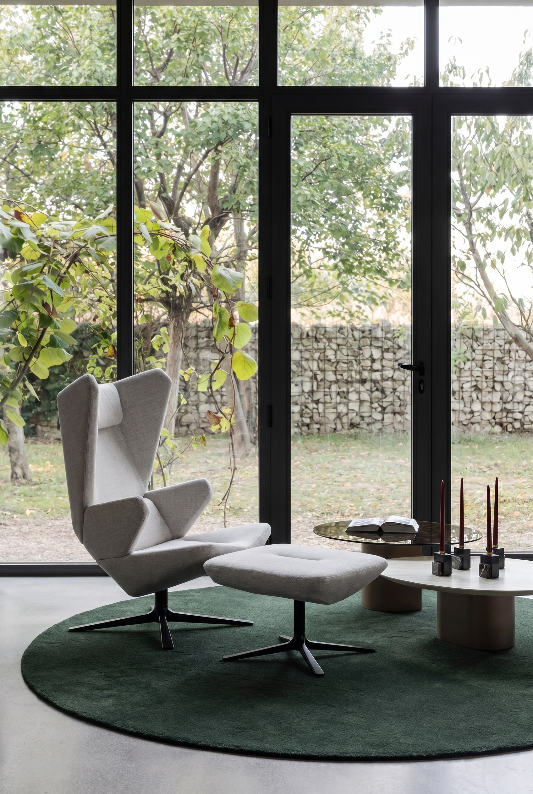 Skulpturaler grauer Sessel mit hohem Rücken auf einem dunkelgrünen runden Teppich in einem minimalistischen Wohnzimmer mit großen Fenstern