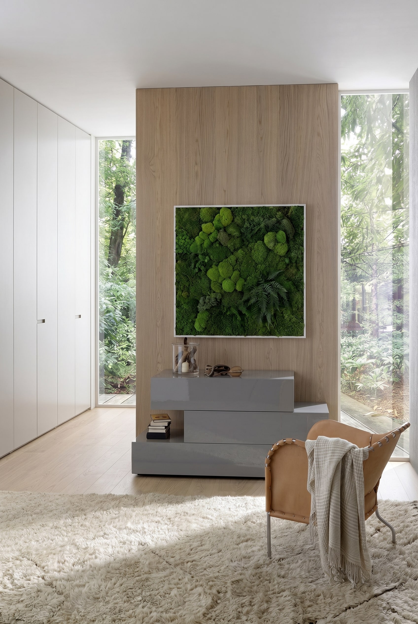 Modernes Schlafzimmer mit grauer, asymmetrischer Kommode in Hochglanz, darüber ein gerahmtes Moosbild und ein lederner Sessel